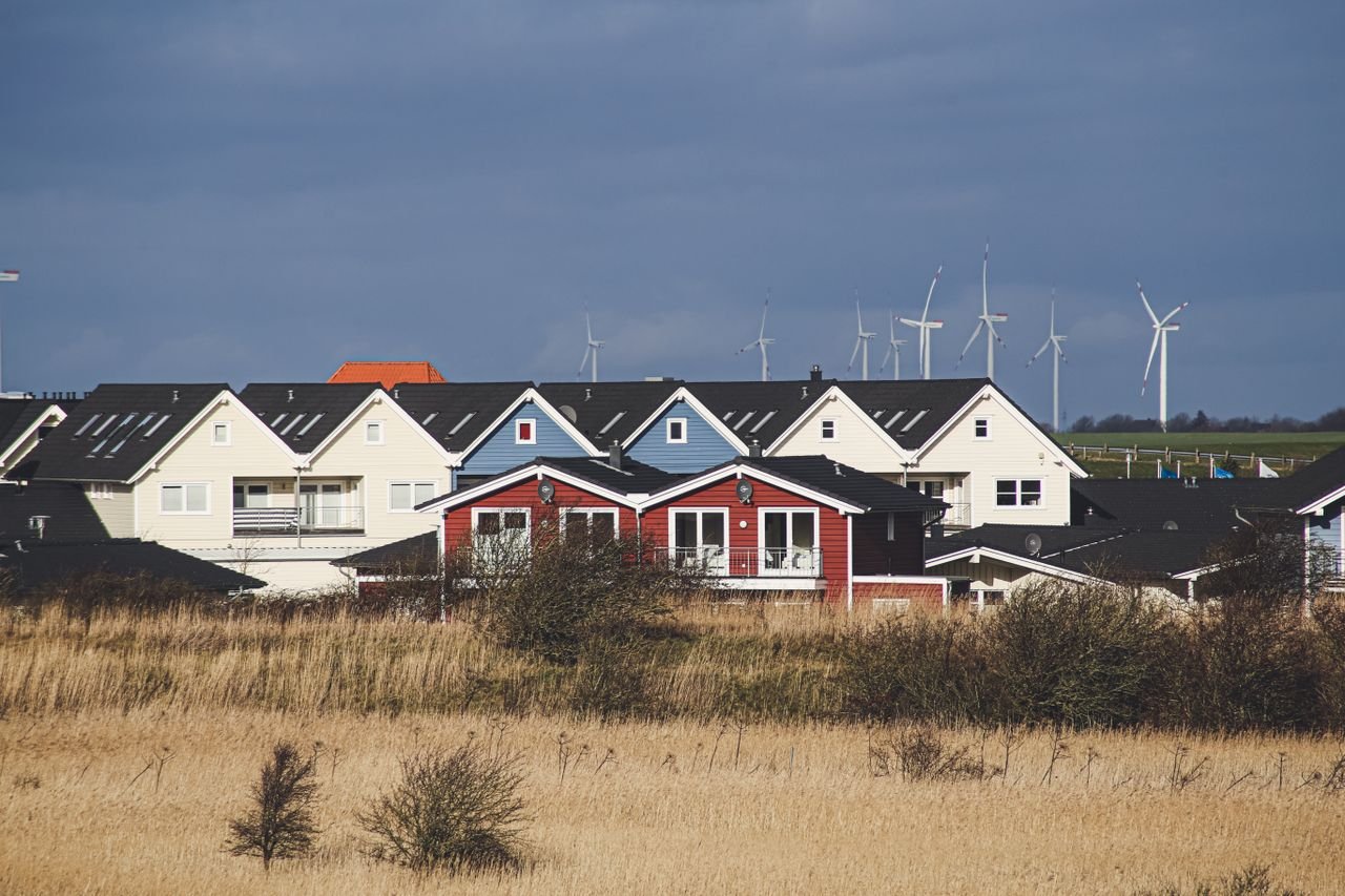 our-story Charming rural houses with wind turbines in Dagebüll, Germany under cloudy skies.